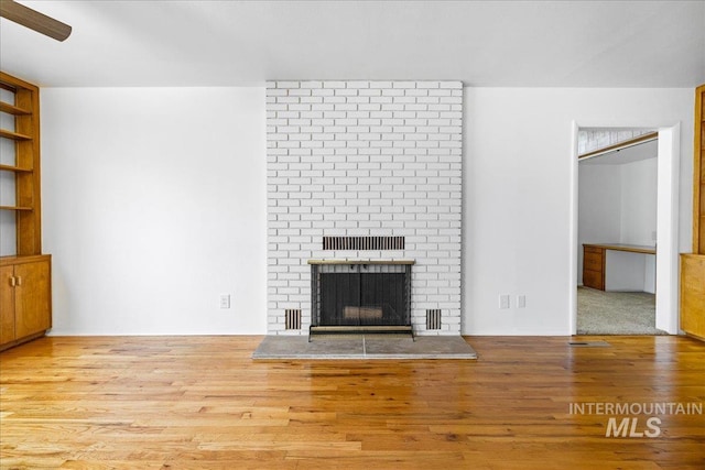 unfurnished living room with a brick fireplace, wood finished floors, and ceiling fan