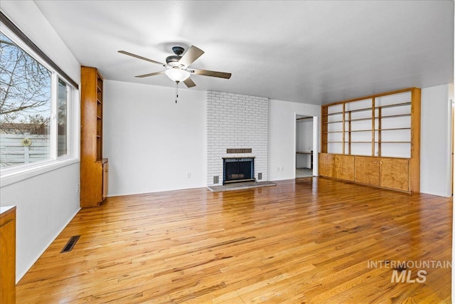 unfurnished living room with visible vents, a brick fireplace, light wood-style flooring, and a ceiling fan