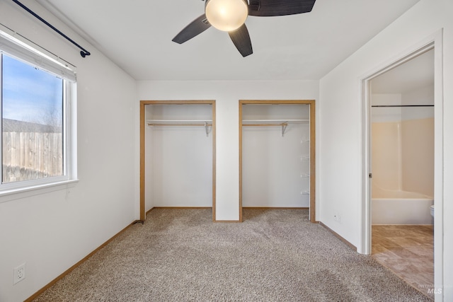 unfurnished bedroom with baseboards, carpet, multiple closets, and ceiling fan