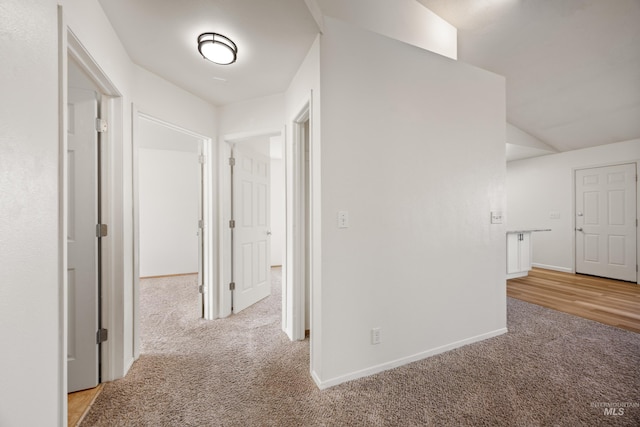 hallway featuring carpet flooring, lofted ceiling, and baseboards