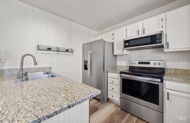 kitchen featuring a sink, appliances with stainless steel finishes, white cabinets, light wood finished floors, and decorative backsplash