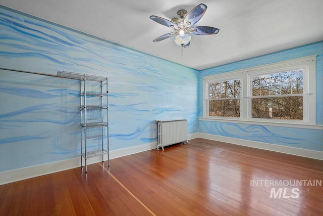 unfurnished room featuring baseboards, a ceiling fan, radiator, and wood finished floors