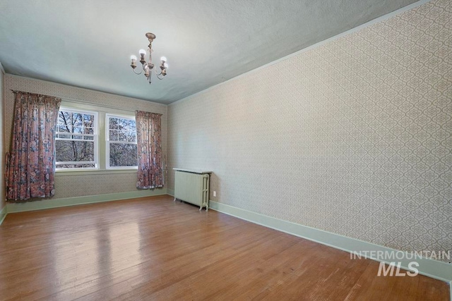 spare room with radiator heating unit, an inviting chandelier, wallpapered walls, and wood finished floors