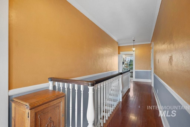 hall featuring dark wood-style flooring, baseboards, ornamental molding, and an upstairs landing