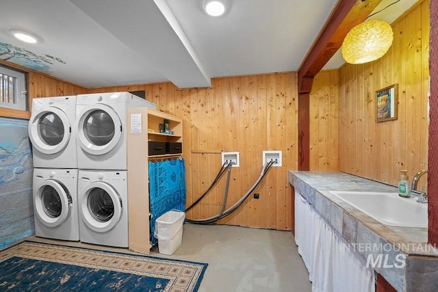washroom featuring washer and dryer, stacked washer and dryer, wood walls, and a sink