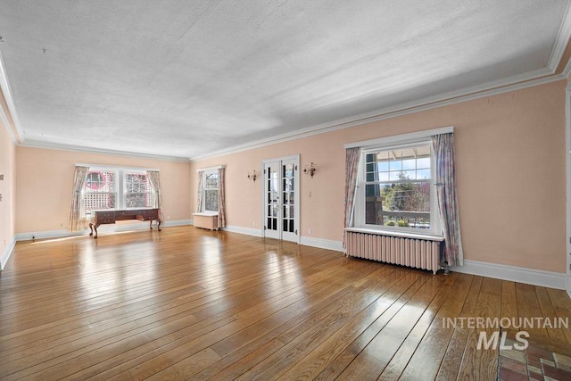 empty room featuring radiator heating unit, wood-type flooring, baseboards, and crown molding