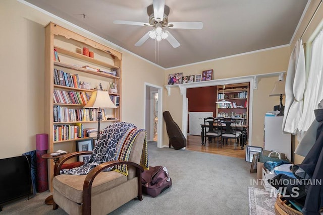 living area featuring ornamental molding, ceiling fan, and carpet