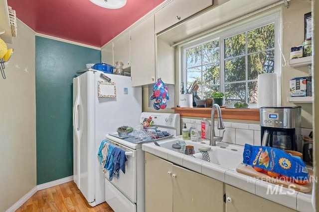 kitchen featuring light wood-style floors, tile countertops, white appliances, a sink, and baseboards