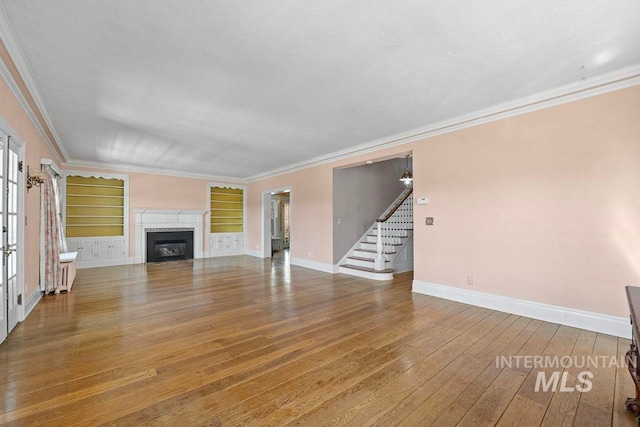 unfurnished living room with stairs, ornamental molding, baseboards, and hardwood / wood-style flooring