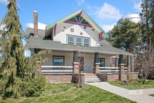 victorian-style house with a chimney, covered porch, and stone siding