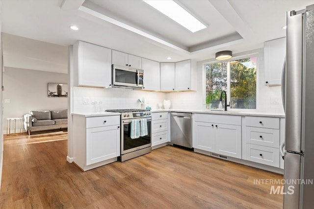 kitchen with a sink, light wood-style floors, a raised ceiling, visible vents, and appliances with stainless steel finishes