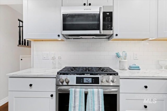 kitchen featuring appliances with stainless steel finishes, white cabinetry, light stone countertops, and backsplash