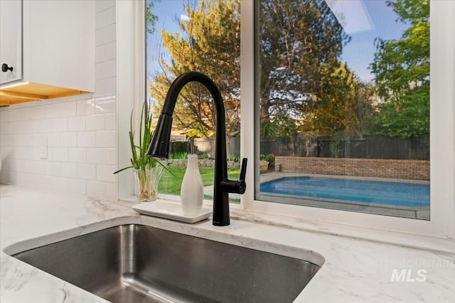 interior details featuring white cabinets, backsplash, light stone counters, and a sink
