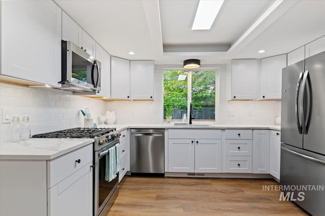 kitchen featuring recessed lighting, appliances with stainless steel finishes, white cabinets, a sink, and a tray ceiling
