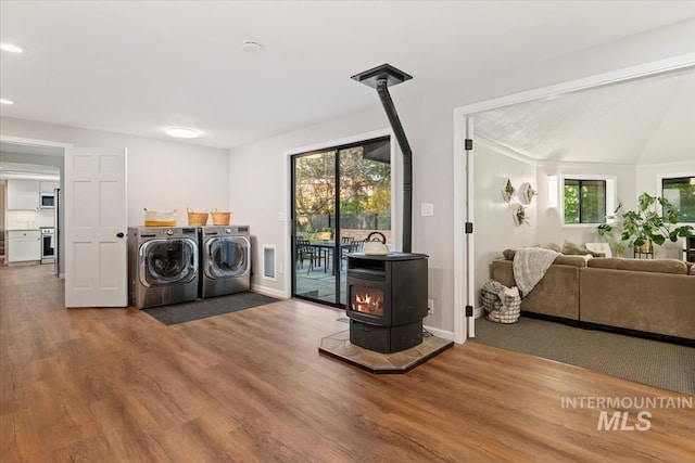 laundry room featuring independent washer and dryer, a wood stove, baseboards, wood finished floors, and laundry area