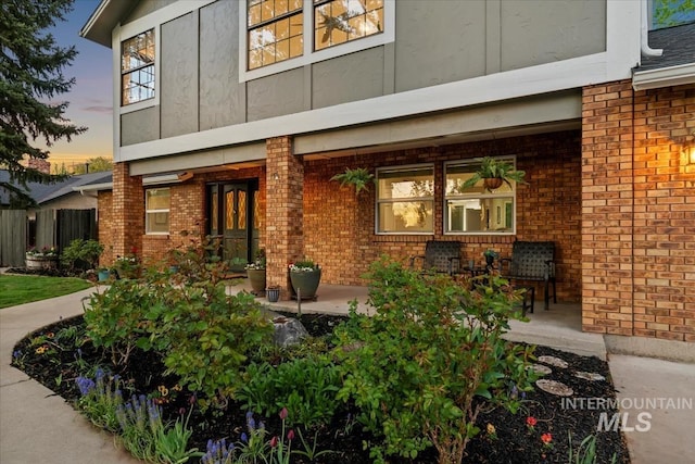 exterior space with covered porch, brick siding, and fence