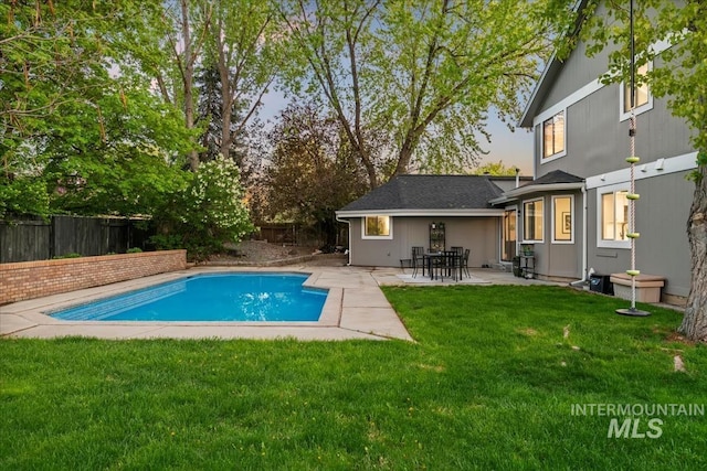 pool at dusk featuring a fenced in pool, a yard, a patio area, and a fenced backyard