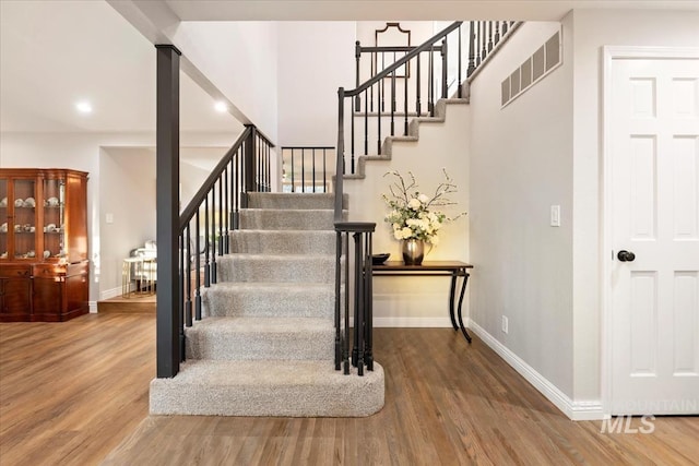 staircase with visible vents, wood finished floors, and baseboards