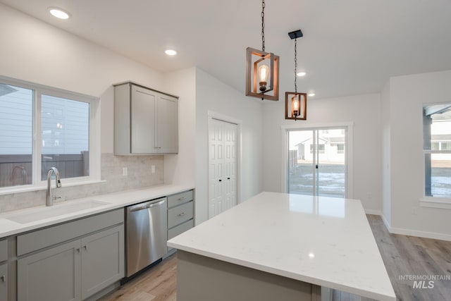 kitchen with a kitchen island, gray cabinets, light wood-type flooring, stainless steel dishwasher, and sink