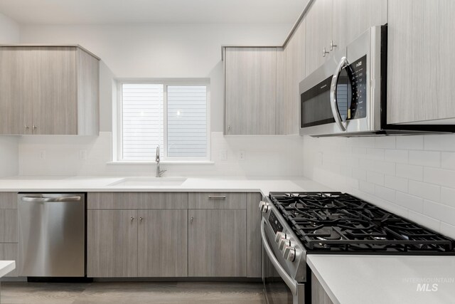 kitchen with hanging light fixtures, sink, gray cabinets, appliances with stainless steel finishes, and light wood-type flooring