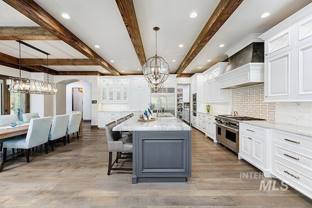 kitchen featuring an inviting chandelier, beamed ceiling, premium range hood, tasteful backsplash, and stainless steel appliances
