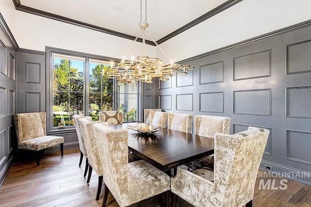 dining space with an inviting chandelier, ornamental molding, wood finished floors, and a decorative wall