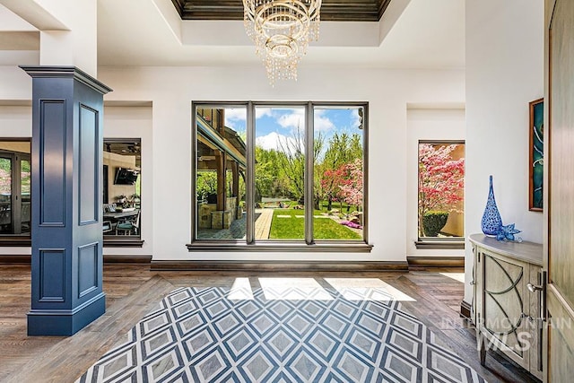 interior space with baseboards, an inviting chandelier, wood finished floors, and a raised ceiling