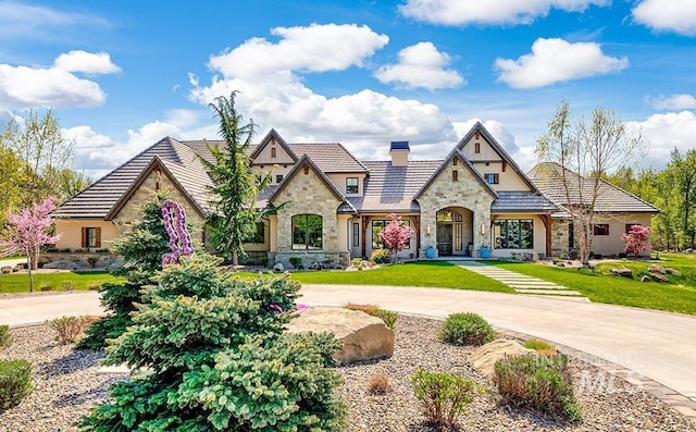 tudor-style house with curved driveway, a chimney, stucco siding, and stone siding