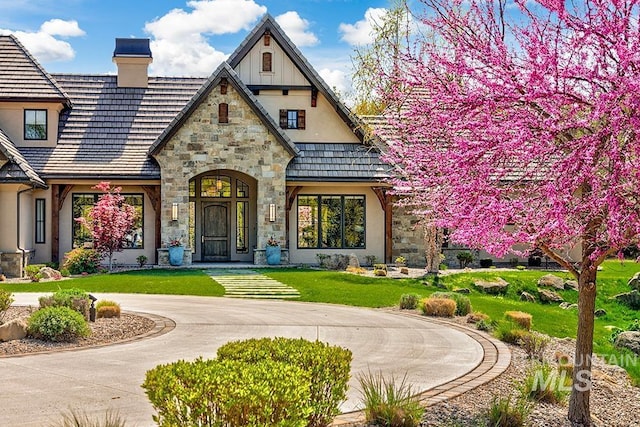 exterior space with stucco siding, a chimney, a front lawn, and stone siding