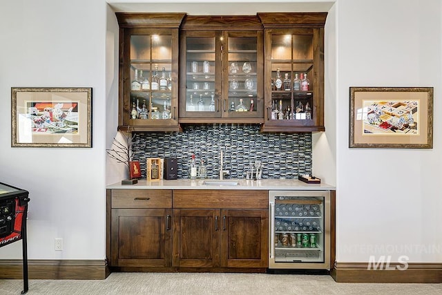 bar with a sink, beverage cooler, indoor wet bar, baseboards, and decorative backsplash
