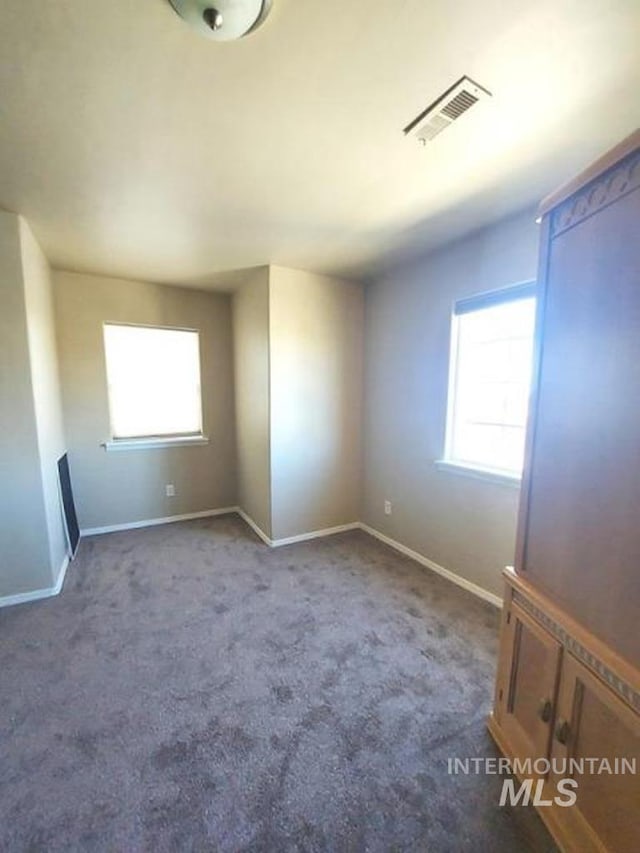 empty room featuring plenty of natural light, baseboards, visible vents, and carpet