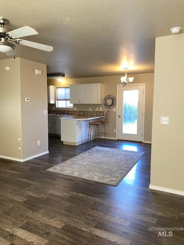 kitchen with white cabinets, dark wood finished floors, a peninsula, and ceiling fan with notable chandelier