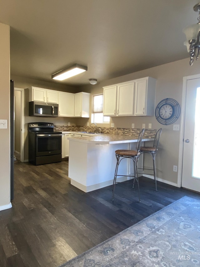 kitchen with stainless steel microwave, range with electric cooktop, dark wood finished floors, and a peninsula