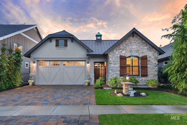 view of front of house featuring a standing seam roof, stucco siding, stone siding, a yard, and driveway