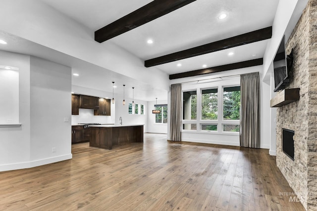 unfurnished living room with a stone fireplace, beamed ceiling, wood-type flooring, a sink, and recessed lighting