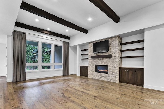 unfurnished living room with beam ceiling, hardwood / wood-style floors, a stone fireplace, baseboards, and recessed lighting
