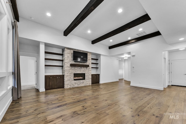 unfurnished living room with hardwood / wood-style flooring, beam ceiling, a stone fireplace, baseboards, and recessed lighting