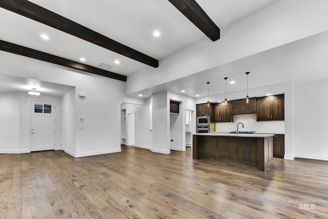 kitchen with appliances with stainless steel finishes, light countertops, beam ceiling, hardwood / wood-style flooring, and dark brown cabinets