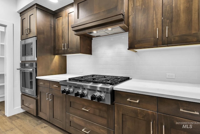 kitchen featuring stainless steel appliances, light wood-type flooring, light countertops, backsplash, and dark brown cabinets