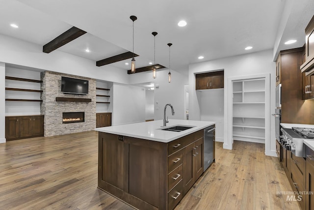 kitchen with a sink, appliances with stainless steel finishes, light wood finished floors, dark brown cabinets, and beam ceiling