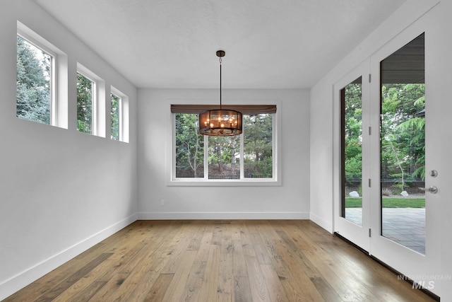 unfurnished dining area featuring plenty of natural light, baseboards, a chandelier, and hardwood / wood-style floors