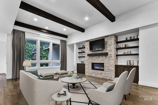living room featuring beam ceiling, wood finished floors, baseboards, a stone fireplace, and recessed lighting