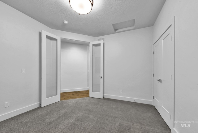 unfurnished bedroom with carpet, attic access, a textured ceiling, and baseboards