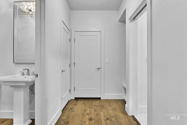 corridor featuring wood finished floors, a sink, and baseboards
