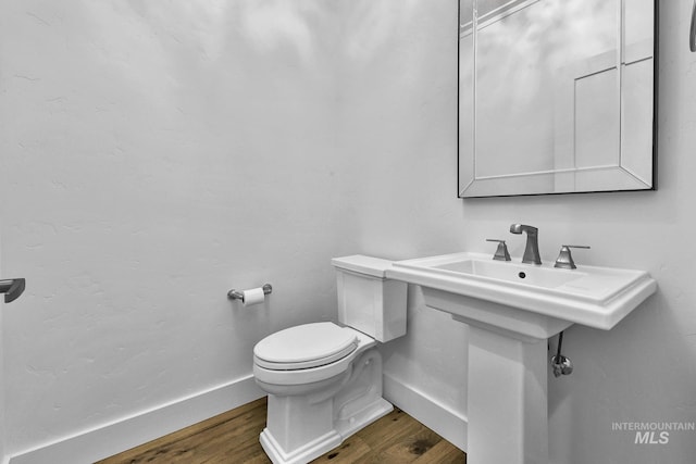 half bathroom featuring wood finished floors, toilet, and baseboards
