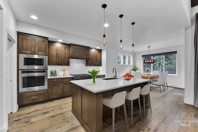 kitchen with stainless steel appliances, a sink, light countertops, light wood-style floors, and recessed lighting