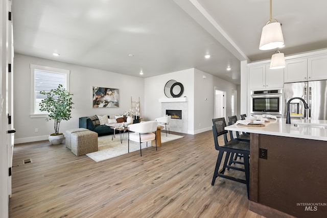 kitchen featuring light wood finished floors, open floor plan, stainless steel refrigerator, light countertops, and a high end fireplace