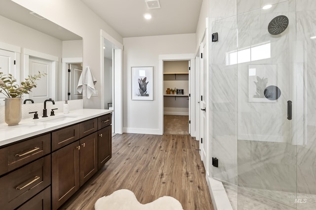 bathroom with a marble finish shower, visible vents, wood finished floors, and vanity