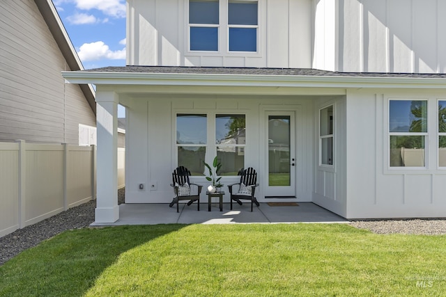 rear view of house with a shingled roof, a lawn, board and batten siding, a patio area, and fence