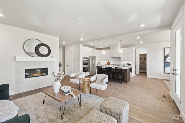 living room featuring a fireplace, recessed lighting, visible vents, light wood-type flooring, and baseboards